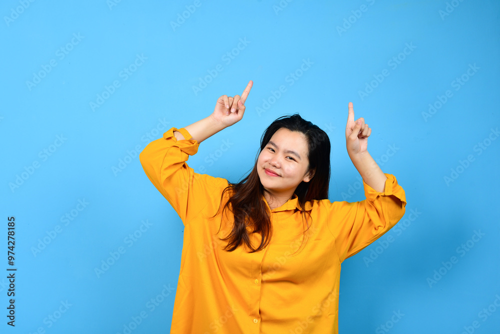 Happy asian woman in orange shirt pointing right side, left side and up side to copy space and looking at the camera isolated blue background Happy asian woman in orange shirt pointing right side, left side and up side to copy space and looking at the camera isolated blue background