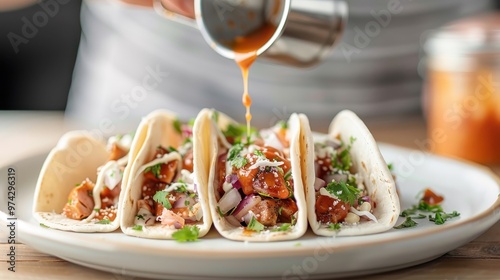 A hand drizzling hot sauce onto a plate of tacos.