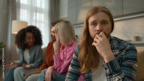 Upset offended Caucasian man male guy thinking anxiety worried think suffer at home feel lonely excluded ignoring friends talking multiracial fun people women men Caucasian buddies introvert avoiding