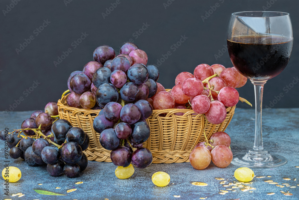 Black grapes on a table, red grapes in a basket and a glass of red wine on the table