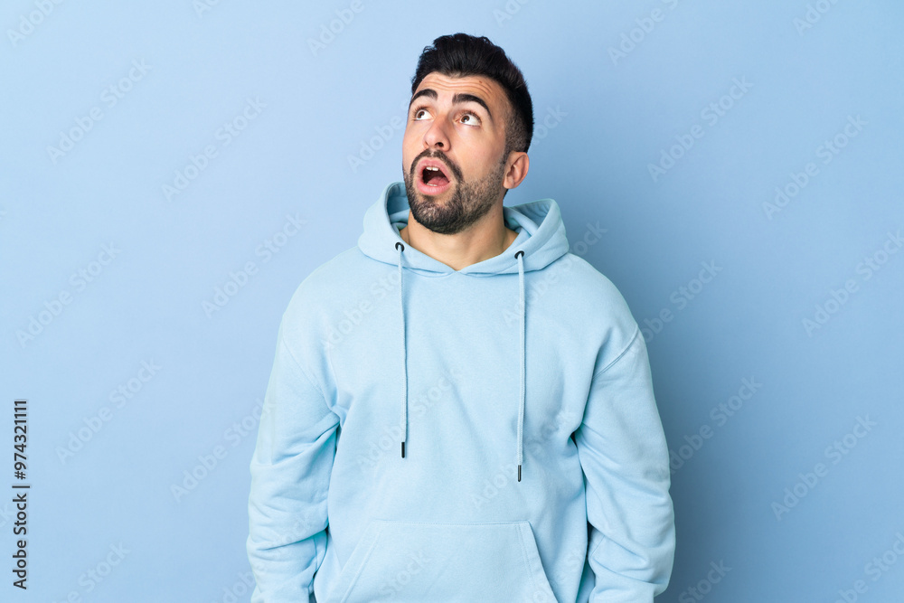Caucasian man over isolated blue background looking up and with surprised expression Caucasian man over isolated blue background looking up and with surprised expression