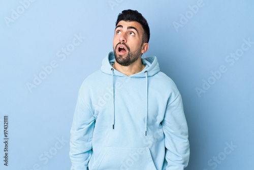 Caucasian man over isolated blue background looking up and with surprised expression