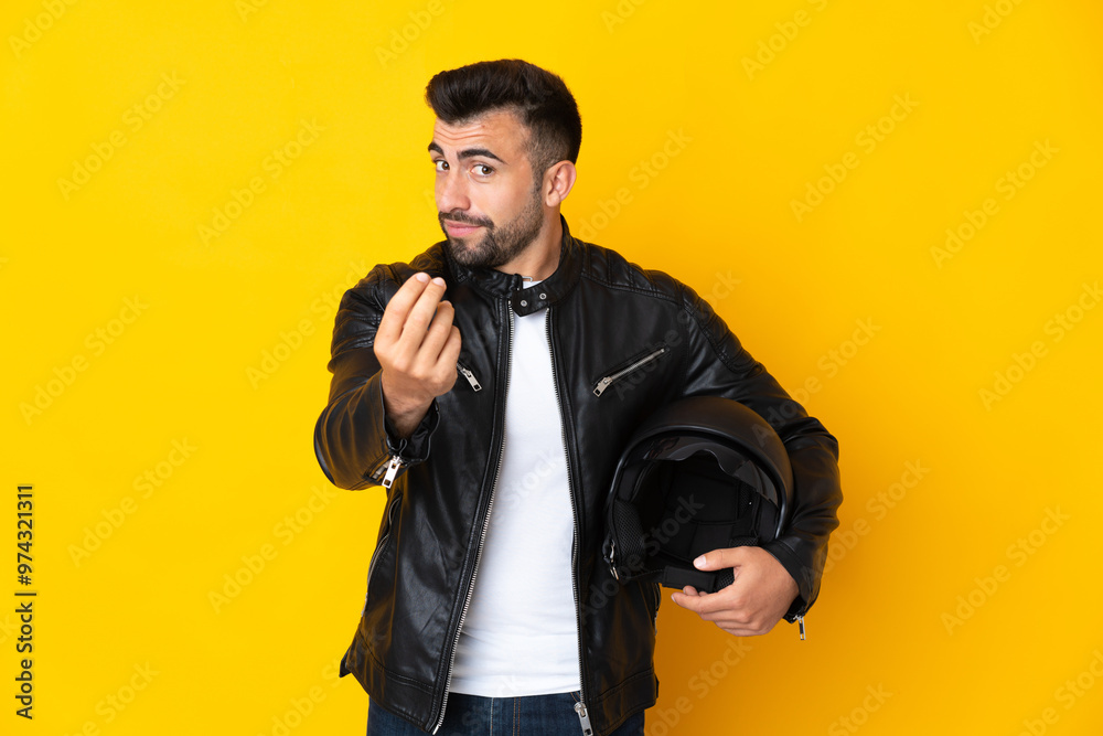Caucasian man with a motorcycle helmet over isolated yellow background making money gesture Caucasian man with a motorcycle helmet over isolated yellow background making money gesture