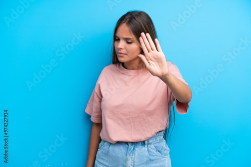 Young caucasian woman isolated on blue background making stop gesture and disappointed