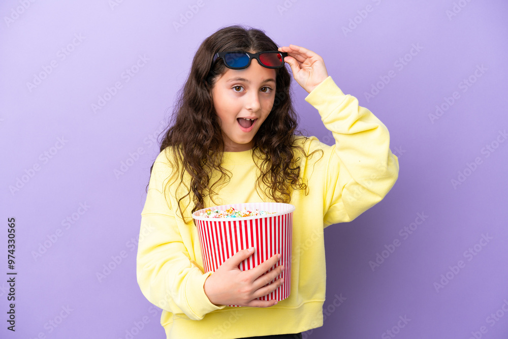 Little caucasian girl isolated on purple background surprised with 3d glasses and holding a big bucket of popcorns Little caucasian girl isolated on purple background surprised with 3d glasses and holding a big bucket of popcorns