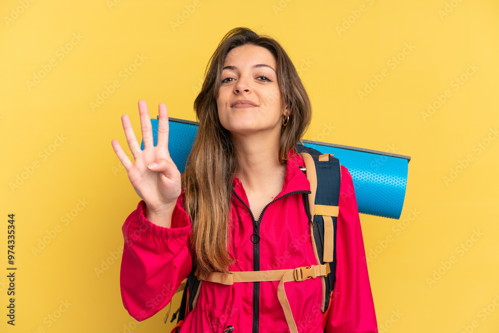 Young mountaineer man with a big backpack isolated on yellow background happy and counting four with fingers Young mountaineer man with a big backpack isolated on yellow background happy and counting four with fingers