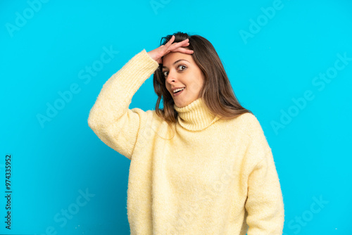 Young caucasian woman isolated on blue background doing surprise gesture while looking to the side