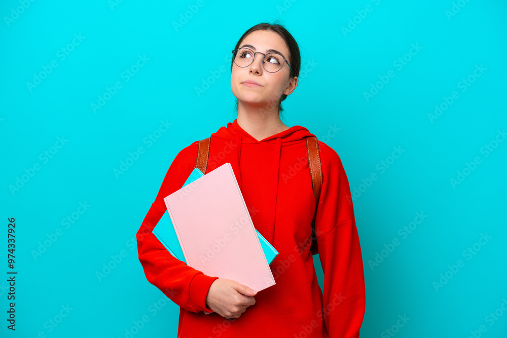 Young student caucasian woman isolated on blue background and looking up Young student caucasian woman isolated on blue background and looking up