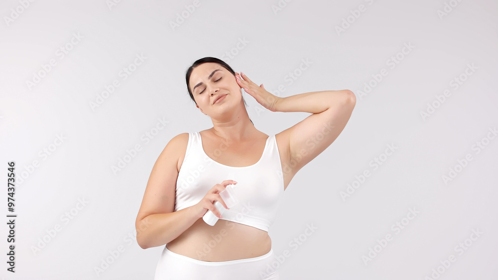 Obraz premium Young, beautiful brunette with curvy figure using skincare products on a white background. Perfect for promoting skincare, emphasizing confidence and beauty with your products.