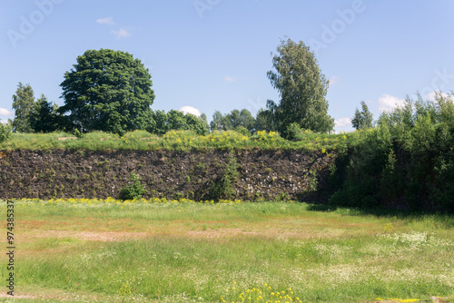 sunny landscape with stone wall among grass, ruins of ancient fortifications