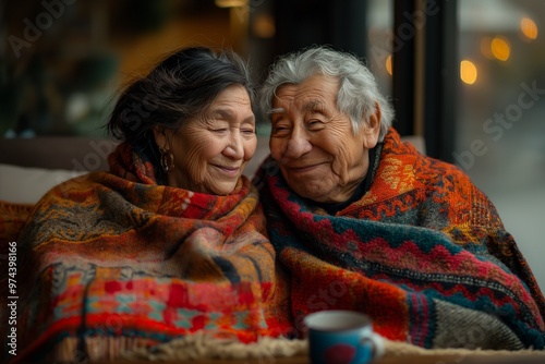 An elderly couple sharing a warm moment wrapped in colorful blankets, smiling fondly at each other.