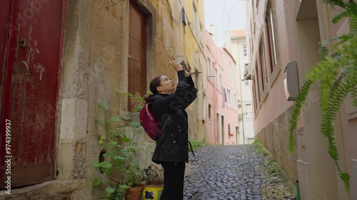 Female tourist or art student takes photos with smartphone in Lisbon street. Visiting Portugal walking around and photographing beautiful architecture and objects in city. Narrow and colorful alleyway