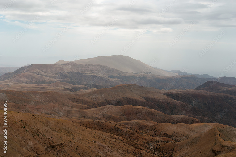 Naklejka premium Layers of mountains are creating a beautiful scenery in a remote area. The brown color of the soil is contrasting with the cloudy sky