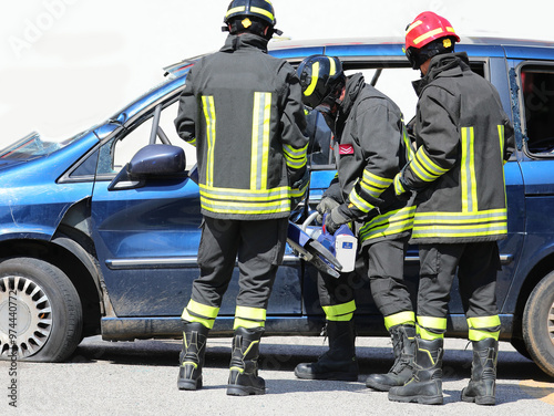 Team of firefighters using the industrial shears called Jaws of Life to free the injured from the crashed car