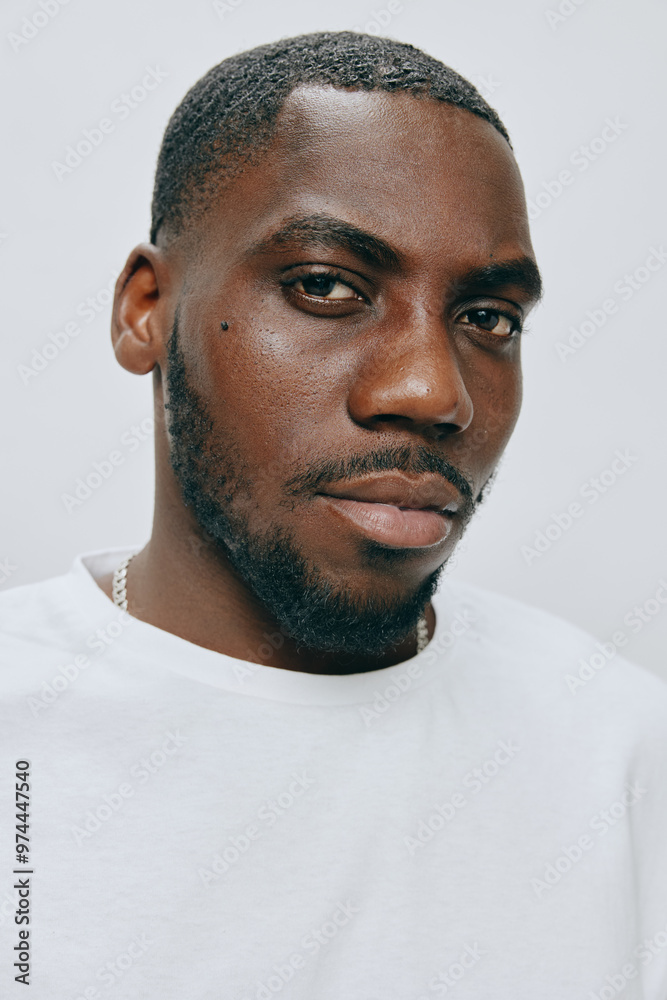 Obraz premium Portrait of a male model with a neutral expression, wearing a white t shirt, set against a light gray background, highlighting modern fashion and self confidence