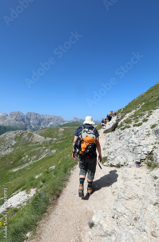 hiker with backpack and hat walking on trail on dolomites mountains in italian alps