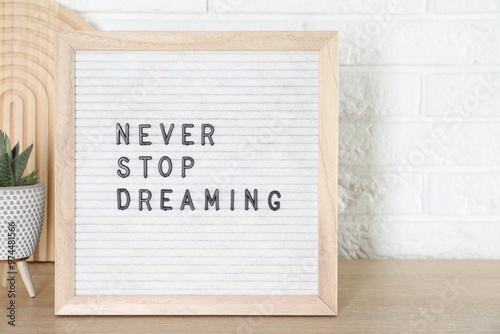 Letter board with phrase Never Stop Dreaming and plant on wooden table near white brick wall