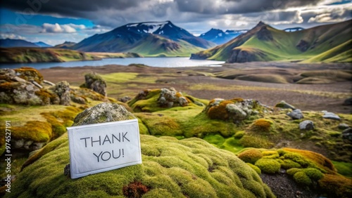 Breathtaking Icelandic landscapes serve as a stunning backdrop for a delicate handwritten thank you note placed gently on a moss-covered rock amidst serene wilderness surroundings. photo