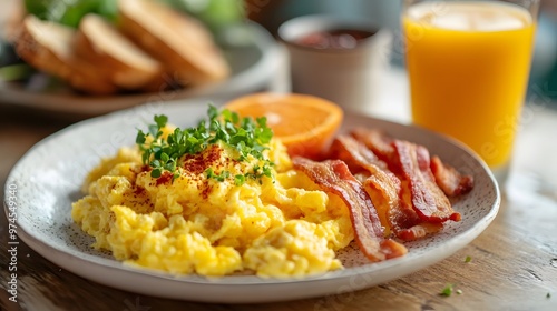 Bright breakfast scene featuring fluffy scrambled eggs, crispy bacon, toasted bread, and vibrant orange juice, invitingly presented on a white plate against a warm morning light background.