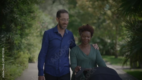 A couple is walking together handinhand with a stroller in a beautiful park setting, photo