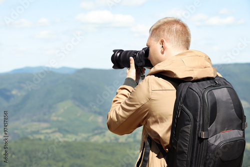 Photographer with backpack and camera taking picture of beautiful mountains, space for text