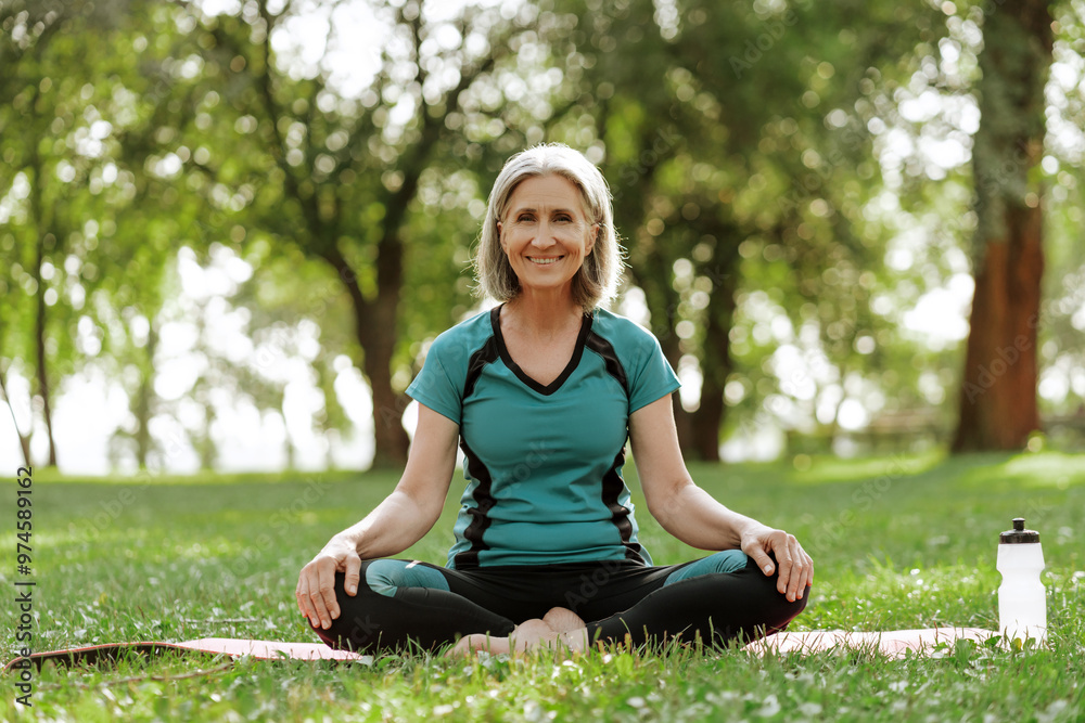 Smiling beautiful senior woman practicing yoga in park sitting on yoga mat, outdoors