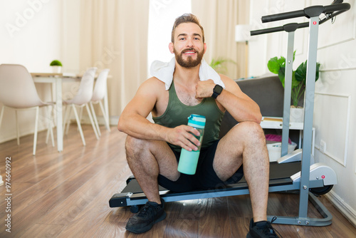 Fit man hydrating with water after a treadmill workout in his home