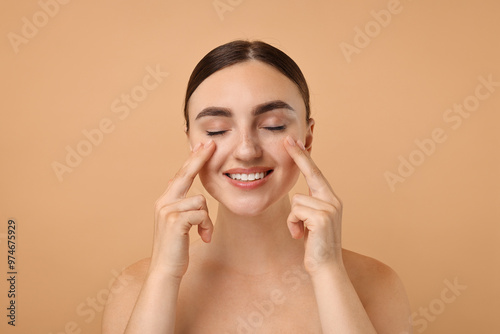 Beautiful young woman doing facial massage on beige background