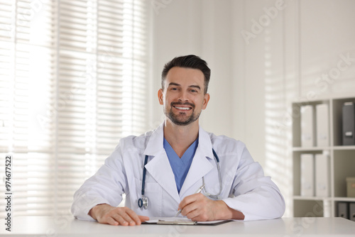 Smiling doctor with clipboard at table in clinic