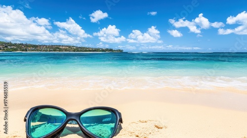 A serene beach scene with sunglasses resting on the sand, showcasing clear waters and blue skies.