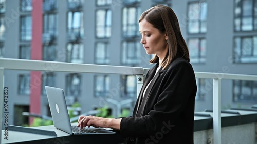 Young serious businesswoman typing on laptop, outdoor urban style