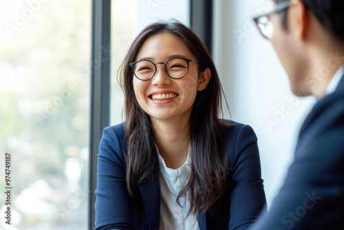 A Chinese businesswoman in her 30s  wearing glasses  is happily smiling while sitting in her office in front of a window.