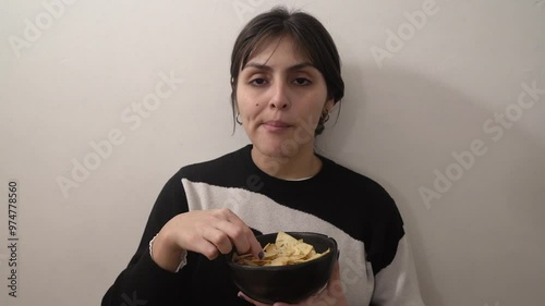 Eating junk food. Closeup view of a young latin american woman eating a bowl with chips with a white background
