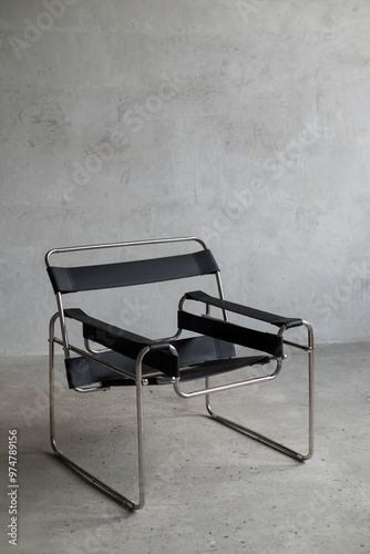 Modern black leather chair with a chrome frame in a minimalist interior against a concrete wall background.