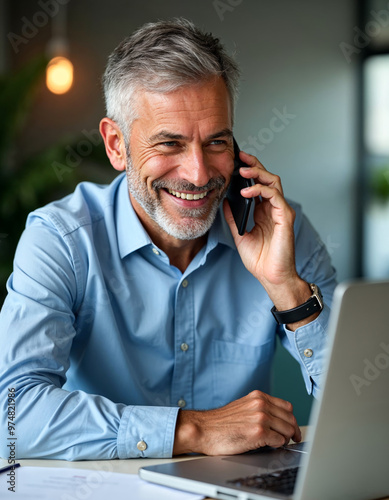 Happy mature businessman talking on mobile phone and using laptop in office work space entrepreneur freelancer small business owner mature professional communication technology cheerful corporate