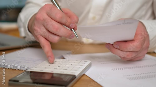 Unrecognizable businessman accountant doing calculation for online financial report at workplace. Serious man using calculator paying bill online holding paper sitting at home office desk. Office desk