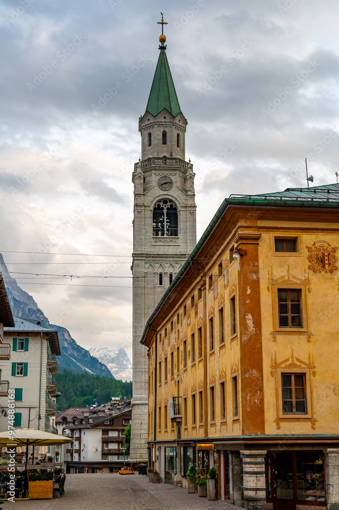 Fototapeta premium A view of the iconic church tower in the heart of Cortina d'Ampezzo. The architectural beauty of the tower stands tall against the backdrop of the surrounding Alpine scenery