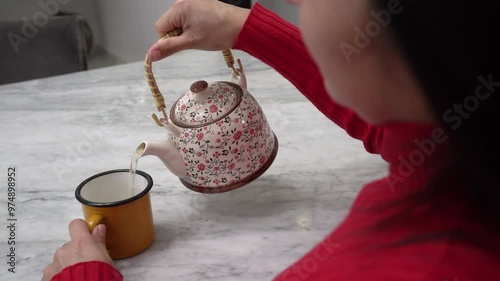 Serving tea. Closeup view of a woman pouring hot tea from a traditional teapot into a cup photo