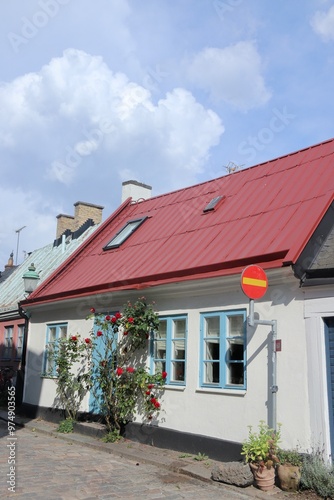Scandinavian Summer House with Red Roof and Roses on a Sunny Cobblestone Street