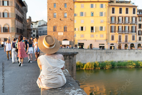 Tourist with hat sitting at sunset on the Holy Trinity Bridge in Florence, Tuscany photo