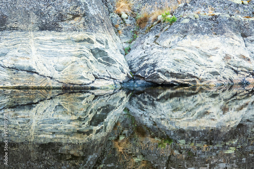 Close-up of grey granite coastal cliff with crevice. There is beautiful texture of grey stone and reflection in water. Background. photo