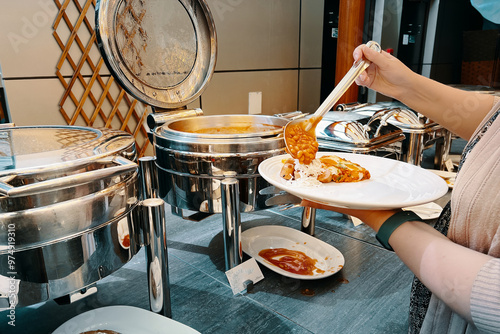 At the hotel buffet, a woman loads her plate with food from a warming machine.