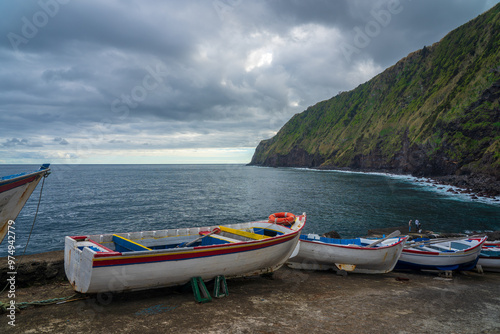 Few boats parked in front of Atlantic Ocean and tall green cliffs near Nordeste village on Sao Miguel island in Azores archipelago