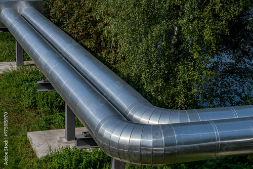 large silver metal pipes for district heating with green leaves in the background photo