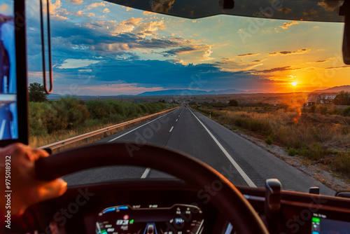 Valokuva View from the driver's seat of a truck on a highway at dawn with the sun on the horizon and a dramatic sky