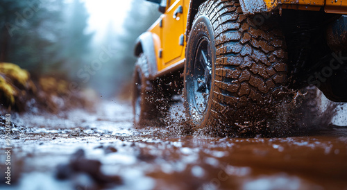 A yellow jeep is driving through a muddy road. The tires are covered in mud and the vehicle is splashing water everywhere. Concept of adventure and excitement