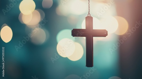 Silver christian cross is hanging against a blue background with light bokeh. The image evokes spirituality, hope and faith