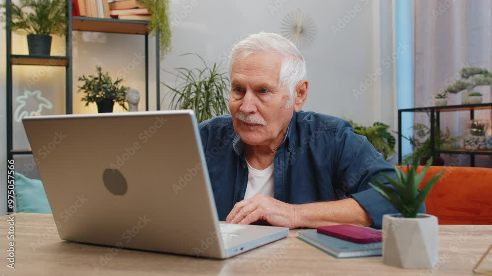 Happy senior man sitting on sofa at table working on laptop pc at office home room. Elderly mature grandfather pensioner freelancer online remote job. E-learning browsing internet on notebook computer Happy senior man sitting on sofa at table working on laptop pc at office home room. Elderly mature grandfather pensioner freelancer online remote job. E-learning browsing internet on notebook computer