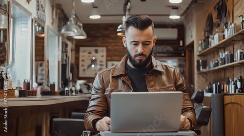 Bearded Man in Brown Leather Jacket Using a Laptop in a Barber Shop