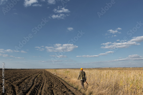 Mature man hunter with gun while walking on field.